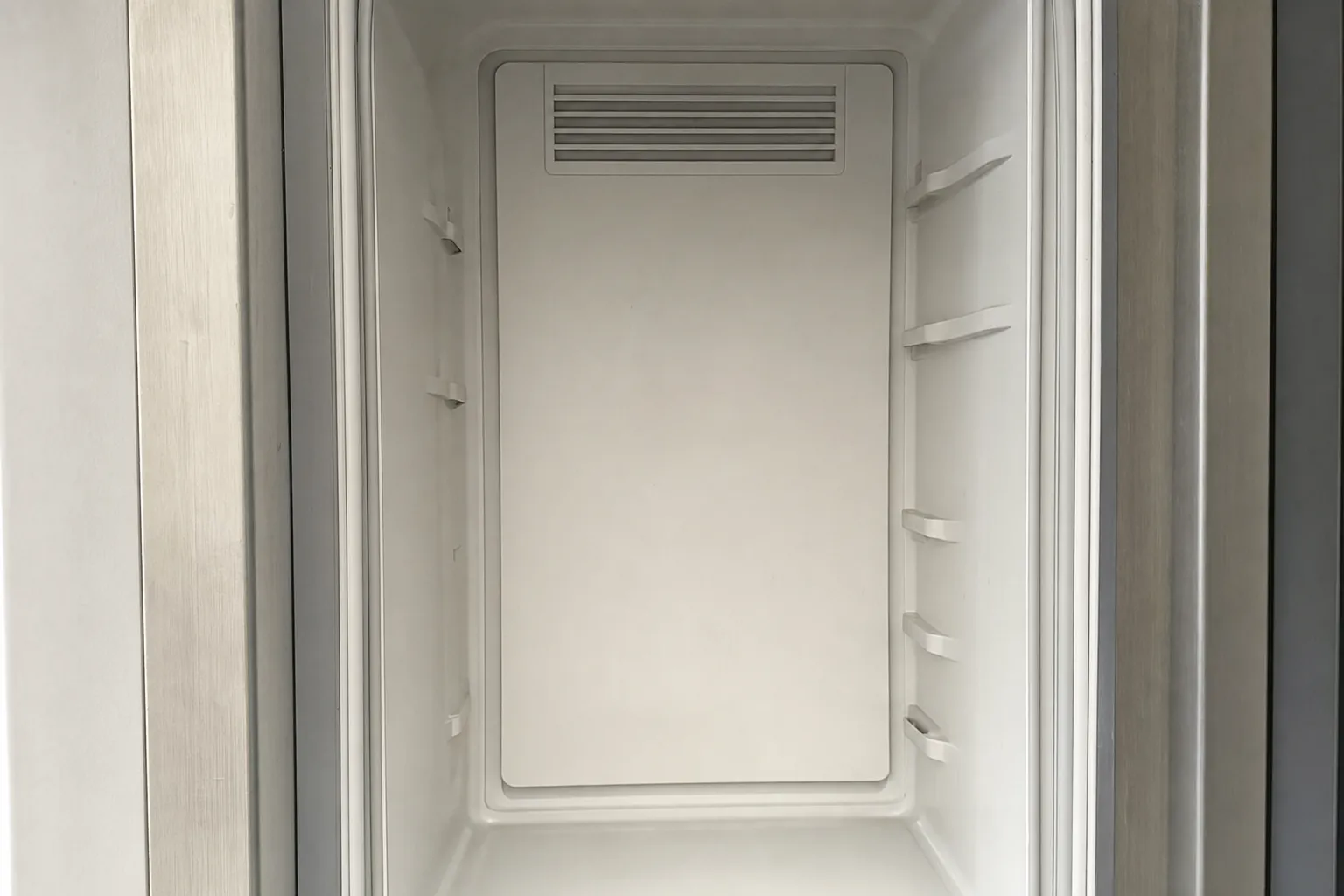 Empty refrigerator cabinet interior, closed up and clean, showing the rear air vent and shelf clips